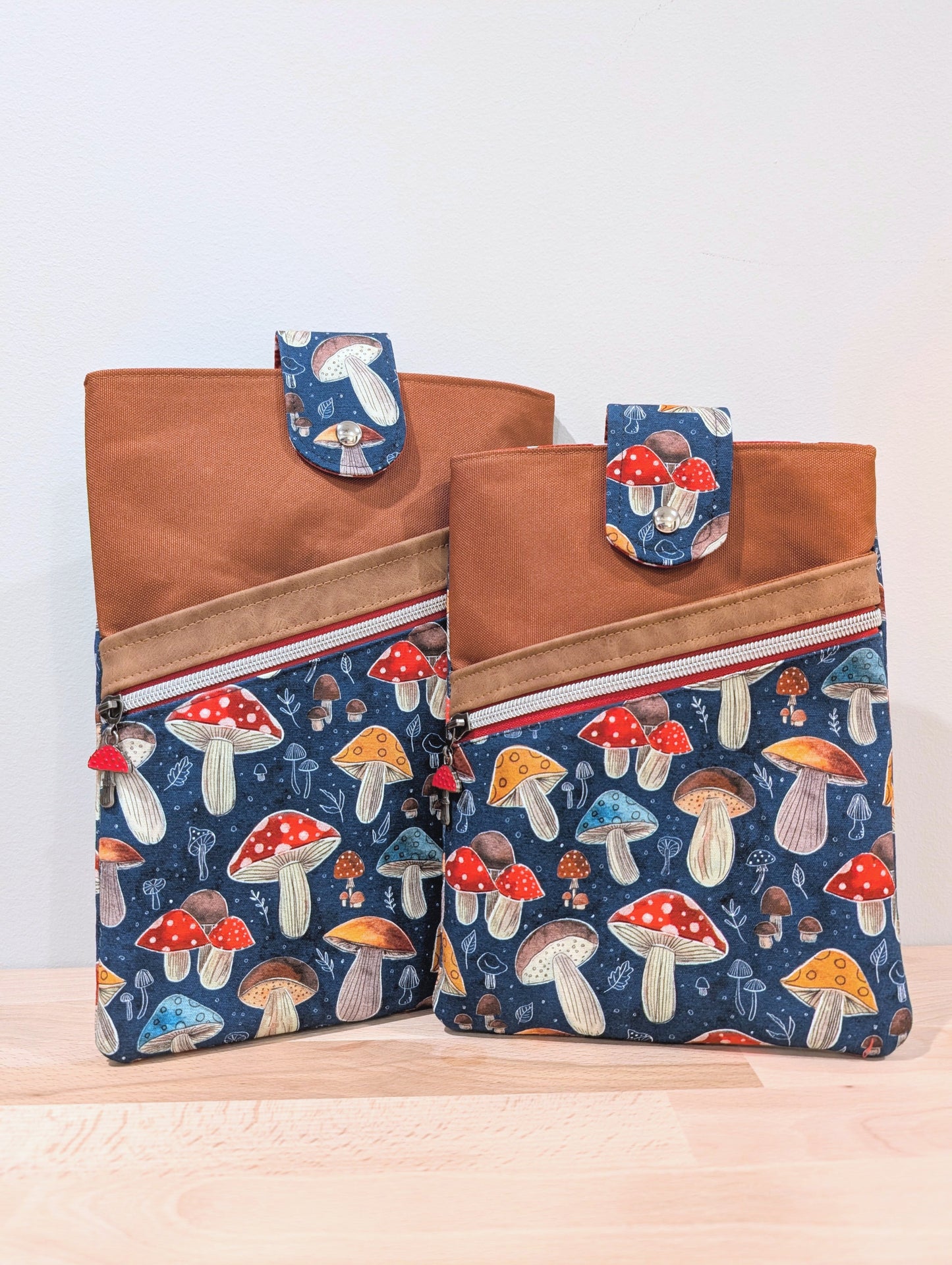 Two fabric sleeves of different sizes with brown, a diagonal red zipper with sliver teeth, a red mushroom zipper pull, and blue mushroom-print lower panels.